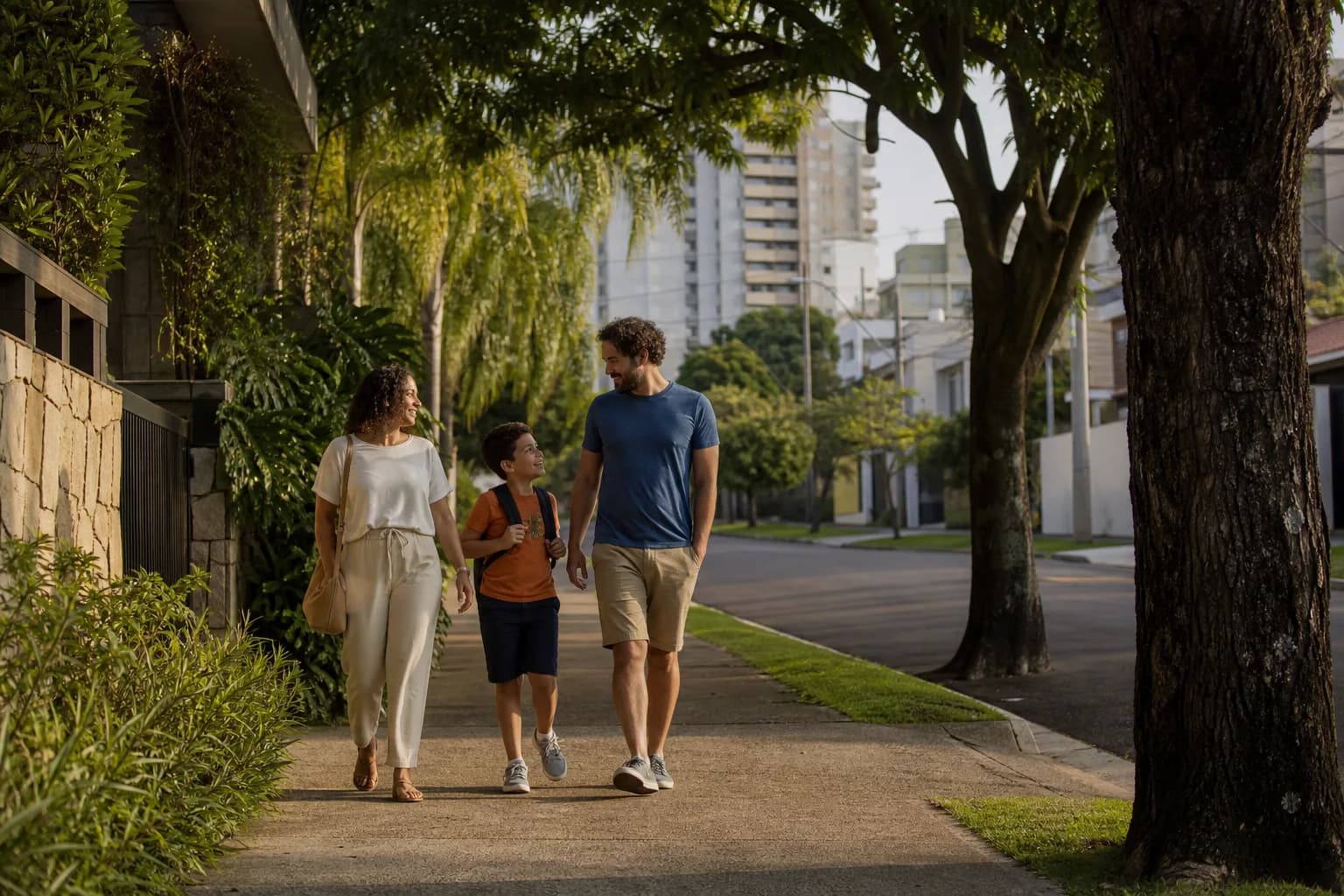 Família caminhando por uma rua residencial arborizada no fim da tarde